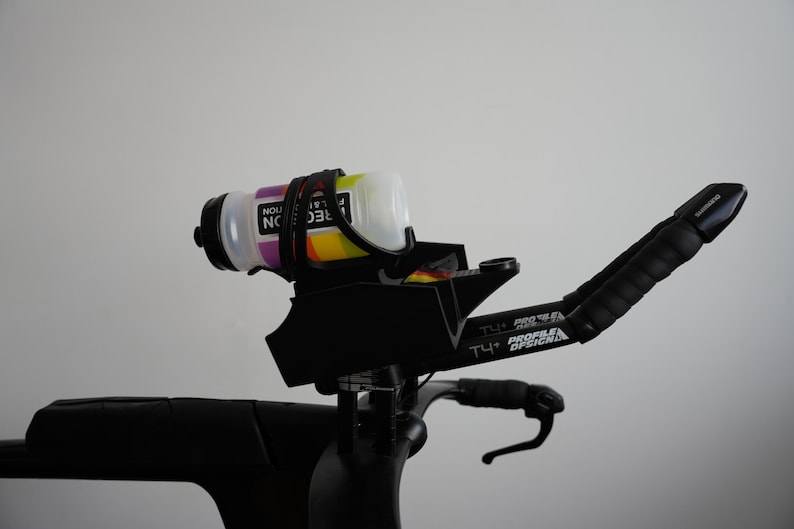 Pu&ograve; includere: Un sistema di appendici aerodinamiche nero per bicicletta con portaborraccia montato e una borraccia bianca con grafiche colorate. Le appendici riportano la scritta T4+ Profile Design e includono nastro adesivo nero sulle impugnature e un supporto.