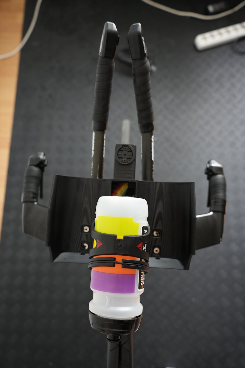 Pu&ograve; includere: Un set di appendici aerodinamiche nere per bicicletta con un portaborraccia centrale nero che sostiene una borraccia bianca con bande orizzontali gialle, arancioni e viola. Il montaggio include due barre di estensione nere con nastro adesivo.