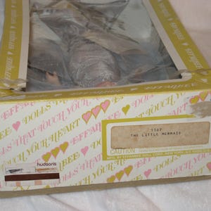 May include: A vintage Effanbee doll box, with a mermaid doll inside. The box is white with pink hearts and the text "Dolls That Touch Your Heart". The label reads "The Little Mermaid".