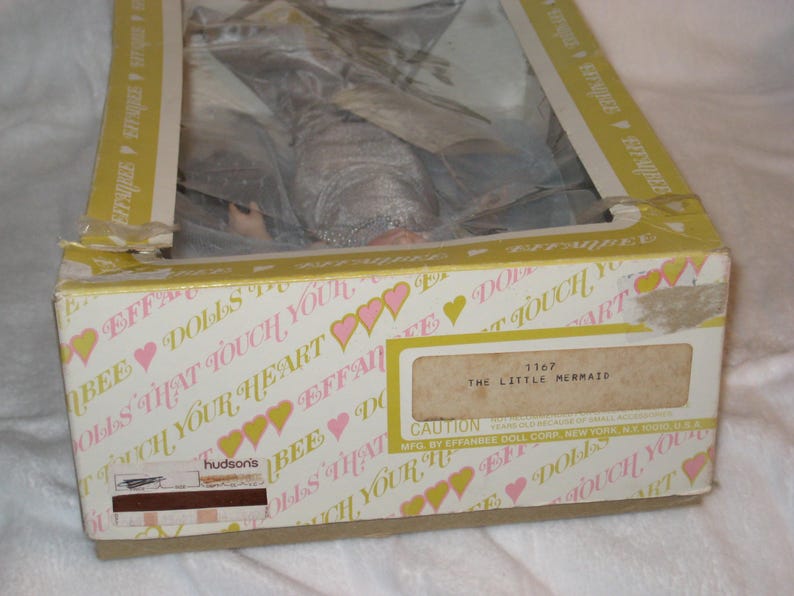 May include: A vintage Effanbee doll box, with a mermaid doll inside. The box is white with pink hearts and the text "Dolls That Touch Your Heart". The label reads "The Little Mermaid".