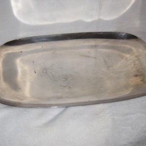 May include: A rectangular silver-colored serving tray with rounded corners. The tray has a slightly raised edge and a polished surface. The tray is likely made of metal and is suitable for serving food or displaying items.