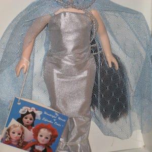 May include: A vintage Effanbee doll in a silver gown with a matching cape and a pearl necklace. The doll has a tag that reads "The Wonderful World of Effanbee Dolls". The doll is in a box.