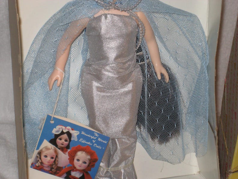 May include: A vintage Effanbee doll in a silver gown with a matching cape and a pearl necklace. The doll has a tag that reads "The Wonderful World of Effanbee Dolls". The doll is in a box.