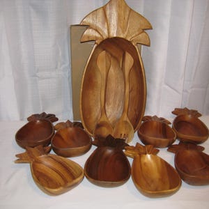 Può includere: Una grande ciotola da portata in legno a forma di ananas con un set di posate da insalata abbinate, accompagnata da otto ciotole individuali più piccole a forma di ananas. Il set presenta una finitura in venature del legno naturale e dettagli intagliati.