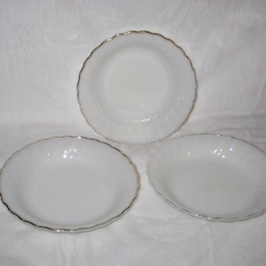 May include: Three white glass bowls with scalloped edges and a silver rim. The bowls are in different shapes, including a round bowl and an oval bowl. The bowls are on a white surface.