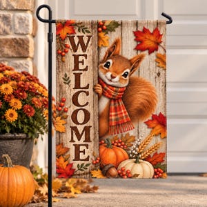 May include: A rectangular garden flag featuring a brown squirrel wearing a plaid scarf, positioned next to a vertical wooden plank with the word WELCOME printed in dark brown letters. The design includes orange pumpkins, red berries, and autumn leaves.