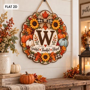 May include: A round wooden wall sign featuring a large letter W, sunflowers, orange and white pumpkins, red maple leaves, and a buffalo plaid bow. The text Grateful Thankful Blessed is printed in black script with small red hearts on a white background.