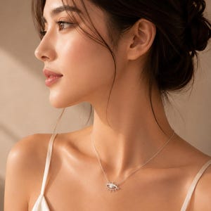 May include: A delicate silver-toned necklace featuring an eye-shaped pendant. The pendant is designed with a central circular element surrounded by radiating lines that resemble eyelashes, suspended from a thin, simple silver-toned chain.