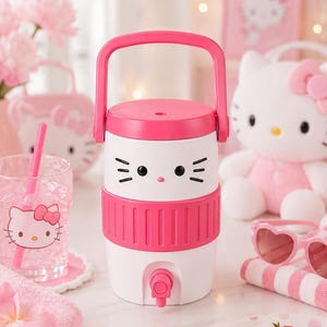 May include: A white and pink beverage dispenser featuring a stylised cat face with black eyes and whiskers, a pink top handle, and a small pink spigot at the base. The cylindrical container has a ribbed pink band around the middle section.