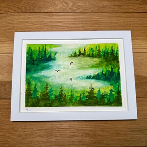 Könnte beinhalten: Gerahmtes Aquarellgemälde einer Waldszene. Das Kunstwerk zeigt einen Fluss, der sich durch üppige grüne Bäume schlängelt, mit drei fliegenden Vögeln. Das Gemälde ist in einem weißen Rahmen gefasst.