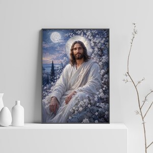 May include: A framed wall art print depicting a figure with long brown hair and a beard, wearing a white robe, seated amidst white flowering trees under a moonlit sky. The artwork features a soft blue and white color palette with a glowing halo.