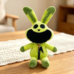 Puede incluir: Un peluche de conejo verde con boca y ojos negros y orejas largas. Lleva un mono verde con un rayo amarillo. El juguete est&aacute; sobre una mesa. El conejo est&aacute; hecho de material suave y est&aacute; dise&ntilde;ado para ni&ntilde;os.