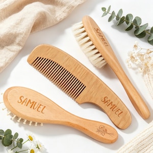 Könnte beinhalten: Ein Set aus drei hellen Holzkämmen und Haarbürsten. Jeder Gegenstand ist mit dem Namen SAMUEL graviert. Eine Bürste hat weiche weiße Borsten, während die andere abgerundete Holzborsten und ein eingraviertes Blumenmotiv aufweist.