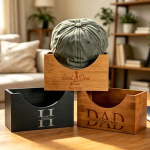 May include: Three wooden boxes with curved fronts sit on a wooden table. One box is black with the name "Hadley" engraved. Another is light brown with "Best Dad" and "Est 2026" engraved. The third box is light brown with "DAD" engraved.