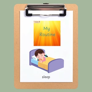 May include: A white card on a brown clipboard featuring the text My Routine and an illustration of a child sleeping in a purple bed with a yellow blanket and a teddy bear. Below the illustration, the word sleep is printed in black text.