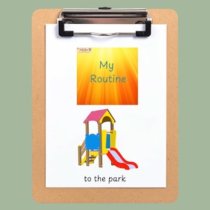 May include: A brown wooden clipboard holding a white card with the text My Routine and to the park. The card features a graphic of a colourful playground structure with a red slide, blue panels, and a yellow roof, set against a bright orange background.
