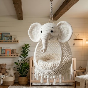 May include: A hanging chair shaped like an elephant head, crafted from off-white crochet yarn. The chair features large ears, a trunk, and a net-like seat with a plush cushion inside. Decorative tassels hang from the bottom edge of the seat.