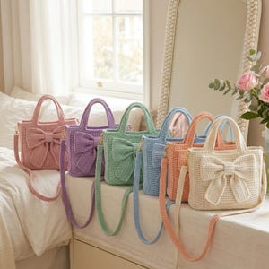 May include: A collection of crochet handbags in various pastel colors, including pink, lavender, mint green, light blue, peach, and cream. Each bag features a large bow detail on the front and a matching crossbody strap.