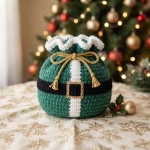 May include: A round, crocheted drawstring pouch in dark green with a white vertical stripe and a black horizontal band featuring a gold-toned rectangular buckle. The top edge is ruffled in white, and a gold cord with tassels ties at the center.