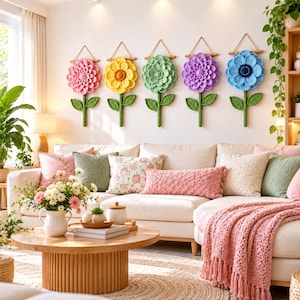 Puede incluir: Cinco decoraciones de pared de flores tejidas a mano en ganchillo, en colores rosa, amarillo, verde claro, morado y azul. Cada flor tiene un centro texturizado, pétalos en capas y un tallo verde con dos hojas, colgadas de un soporte de madera.