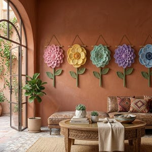 May include: A row of six large, colorful crochet flower wall hangings. Each flower has a different pastel color, including pink, yellow, and blue. The flowers are mounted on a brown wall above a brown leather couch.