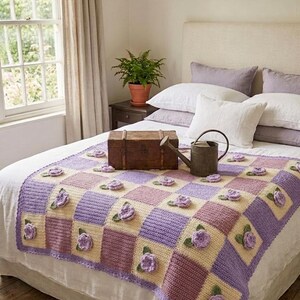 Può includere: Una coperta all'uncinetto fatta a mano con un motivo floreale. La coperta presenta un motivo a scacchiera nei toni del lavanda, crema e malva, con rose all'uncinetto 3D. La coperta è posta su un letto con lenzuola bianche.