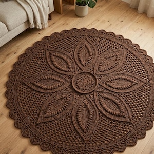 May include: A round, brown crochet rug with a large floral design in the center. The rug features a detailed pattern with a scalloped edge. The rug is made of a soft, textured yarn and is placed on a wooden floor.