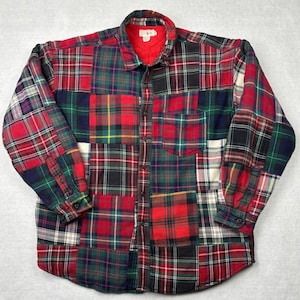 May include: A patchwork flannel shirt in a variety of plaid patterns, featuring red, green, black, and white. The shirt has a button-down front, a collar, and buttoned cuffs. The interior collar is red.