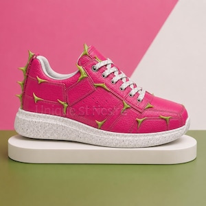 May include: A bright pink sneaker featuring a textured leather upper adorned with protruding lime green thorn-like accents. The shoe includes white speckled rubber soles, white laces with a subtle pattern, and a white interior lining.