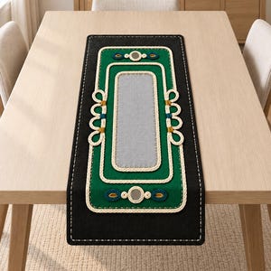 May include: A rectangular table runner featuring a black fabric base with a central light gray panel. The design includes a vibrant green border, intricate cream-colored rope detailing, small circular mirrors, and teal and mustard yellow accents.