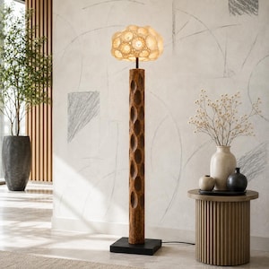 May include: A tall, wooden floor lamp with a carved, cylindrical base and a textured, cream-colored shade. The lamp has a dark brown finish and sits on a black square base. The shade emits a warm glow, creating a cozy ambiance.