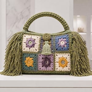May include: A crochet handbag featuring a patchwork of square motifs in shades of olive green, cream, lavender, and mustard yellow. The bag has a thick olive green handle, long fringe detailing on both sides, and a central circular button closure.