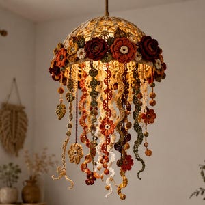 May include: A dome-shaped crochet pendant light fixture featuring a cream-colored base adorned with a ring of dark red, orange, and green crocheted flowers and leaves. Numerous long, dangling crocheted tendrils in autumn colors hang below.