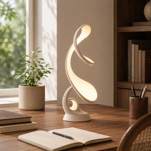 May include: A white table lamp with a curved, abstract, ribbon-like structure that emits a soft, warm glow. The lamp features a smooth, matte finish and a continuous, flowing design that spirals upward from a circular base on a wooden desk.