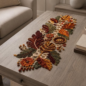 May include: A crochet table runner featuring an intricate arrangement of autumn-themed motifs, including oak and maple leaves in shades of deep burgundy, burnt orange, olive green, and mustard yellow, accented with small cream-colored floral elements.