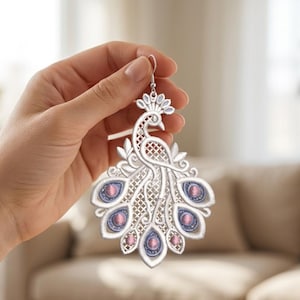 Könnte beinhalten: Silberner Pfau-Ohrring mit aufwendiger filigraner Arbeit und sechs ovalen, rosa und lila Edelsteinen. Der Ohrring wird von einem silbernen Haken gehalten. Das Design ist detailliert und elegant.