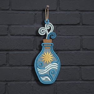 May include: A decorative hanging ornament shaped like a glass bottle with a cork stopper. The design features embroidered blue and white swirling waves, a yellow sun, and light blue vapour rising from the top, all suspended by a jute twine loop.