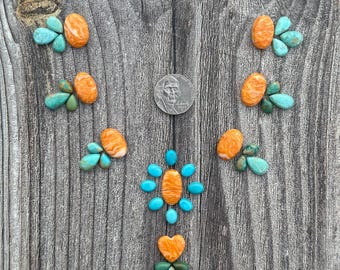 May include: A collection of loose, polished orange spiny oyster shell cabochons and turquoise stones arranged in a V-shape pattern, including a heart-shaped piece and a US nickel for scale, showcasing varied oval and teardrop shapes.