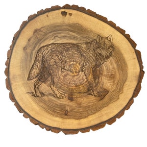 May include: A wood slice with a detailed woodburned image of a wolf. The wood slice is light brown with a dark brown outer edge.