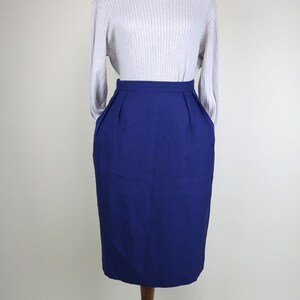 May include: A light gray ribbed turtleneck sweater paired with a knee-length, high-waisted, navy blue pencil skirt. The skirt has pleats at the waist and pockets. The outfit is displayed on a wooden dress form.