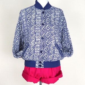 May include: A blue and white patterned bomber jacket with a navy blue collar, cuffs, and buttons. The jacket is paired with bright pink shorts. The clothing is displayed on a mannequin.