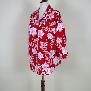May include: A red button-down shirt with a white floral pattern. The short-sleeved shirt is displayed on a mannequin. The shirt's design features large white flowers and leaves, creating a tropical or Hawaiian theme.