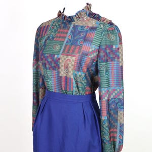 May include: A vintage blouse and skirt set. The blouse features a patchwork pattern with paisley and geometric designs in teal, blue, red, and purple. The skirt is a solid, vibrant blue. The blouse has a ruffled collar and long sleeves.