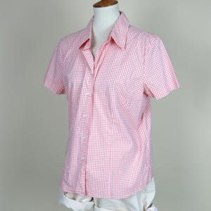 Op de afbeelding: Een roze en witte gingham shirt met korte mouwen op een mannequin. Het shirt heeft een klassieke kraag en een knoopsluiting aan de voorkant. De mannequin draagt ook een witte short. Het shirt is gemaakt van een lichte stof.