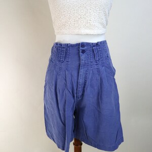 May include: A vintage outfit featuring a white halter top and high-waisted blue shorts. The shorts have a pleated design and button closure. The outfit is displayed on a mannequin.