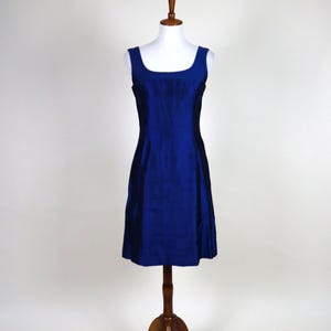 May include: A sleeveless, knee-length, royal blue dress displayed on a wooden dress form. The dress has a square neckline and a slightly A-line silhouette. The dress form is on a wooden stand.