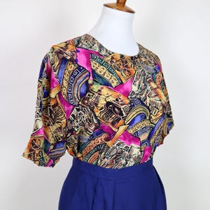 Könnte beinhalten: Ein Vintage-Blusen- und Rock-Set. Die Bluse hat ein farbenfrohes abstraktes Muster mit rosa, gelben, blauen und braunen Farbtönen. Der Rock ist einfarbig tiefblau. Das Outfit wird auf einer Schaufensterpuppe präsentiert.