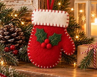 May include: A red felt mitten ornament featuring a white cuff with visible white stitching along the edges. The center of the mitten is decorated with two green felt holly leaves and three small red felt berries attached to the front.