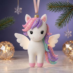 Peut inclure: Une décoration en feutrine représentant une licorne au corps blanc avec des sabots et des ailes roses. La crinière et la queue sont superposées dans des tons rose, violet et bleu sarcelle, ornées de petites paillettes dorées et un ruban rose.