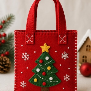 May include: A red felt tote bag featuring a green Christmas tree appliqué with a yellow star topper, white embroidered snowflakes, and small circular accents. The bag has two red handles and white blanket stitching along the edges.